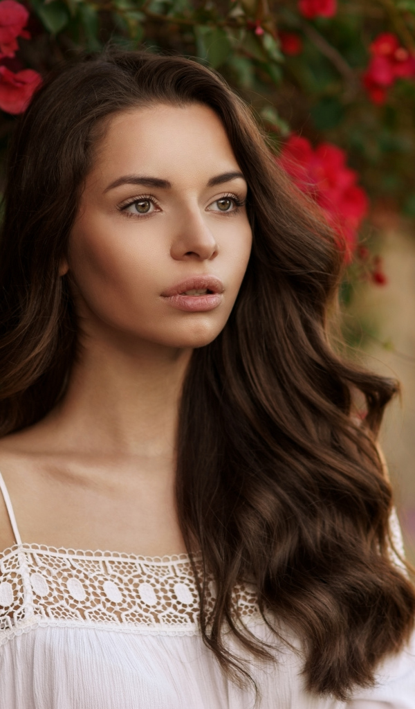 Красивая шатенка у стены на фоне красных цветов