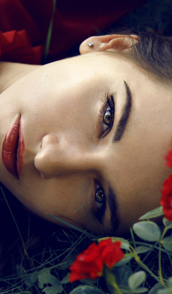 Красивая брюнетка лежит на траве с красными розами