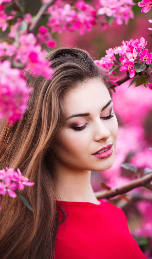 Красивая нежная шатенка у цветущей розовыми цветами ветки
