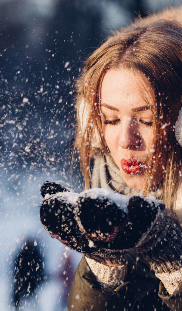 Красивая девушка сдувает снег с ладоней зимой