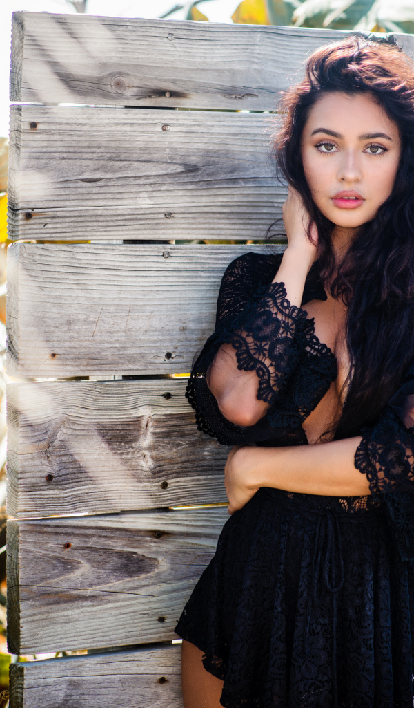 Красивая девушка в черном платье у стены 