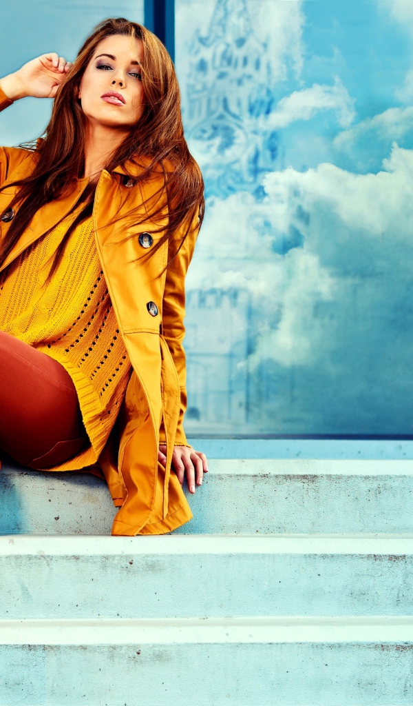 Красивая девушка в пальто сидит на ступеньках