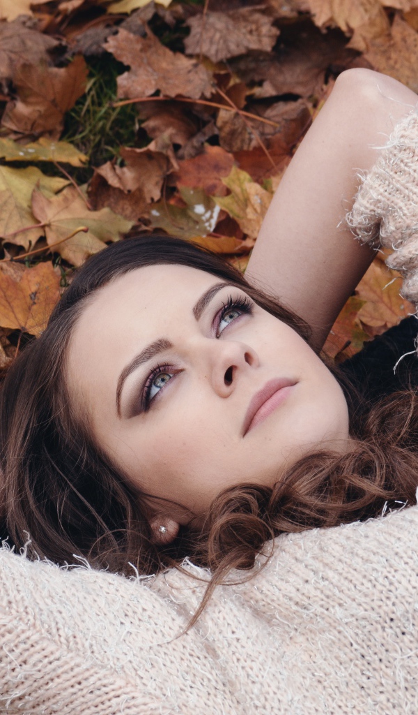 Красивая девушка в свитере лежит на опавших листьях 