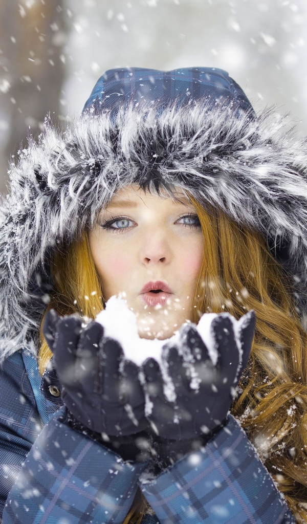 Красивая девушка в теплой куртке со снегом в руках