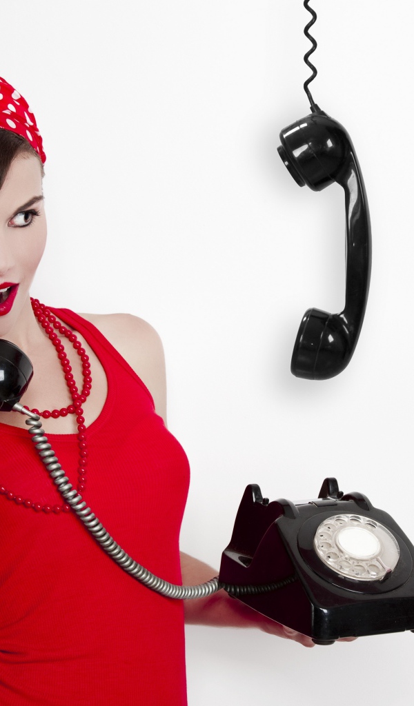 Красивая девушка в красном с черным старым телефоном в руках