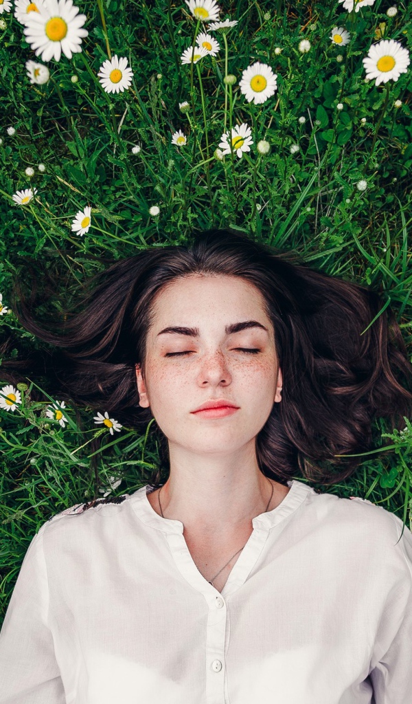 Красивая девушка лежит на зеленой траве с ромашками