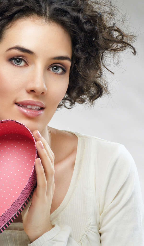 Красивая девушка с коробкой в форме сердца в руках на сером фоне