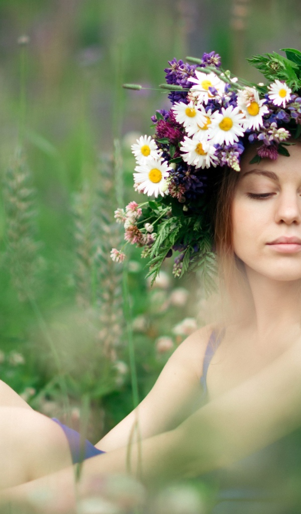 Красивая девушка с венком из полевых цветов на голове летом 