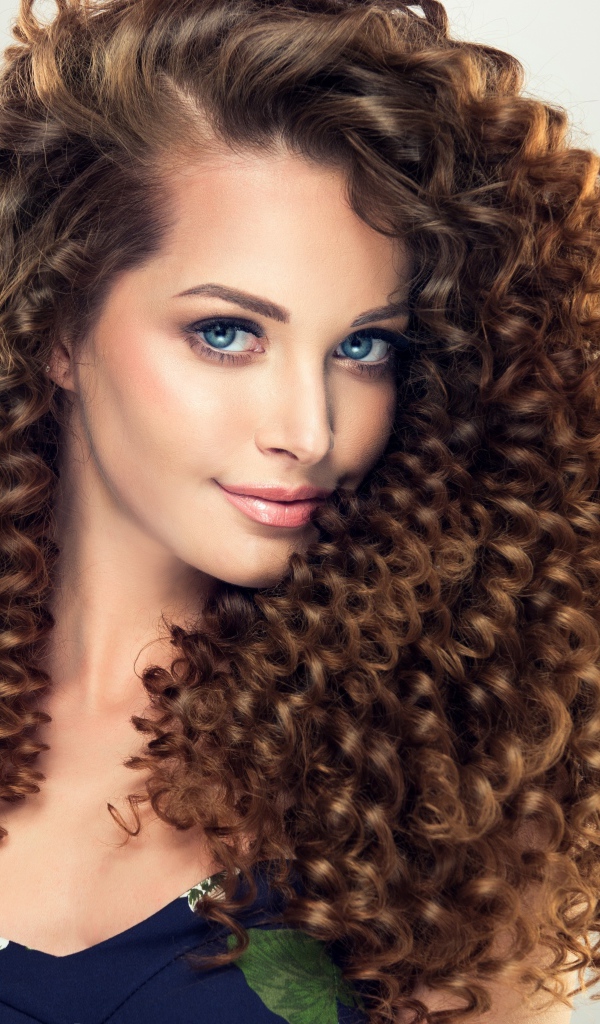 Красивая девушка с длинными волнистыми волосами на сером фоне