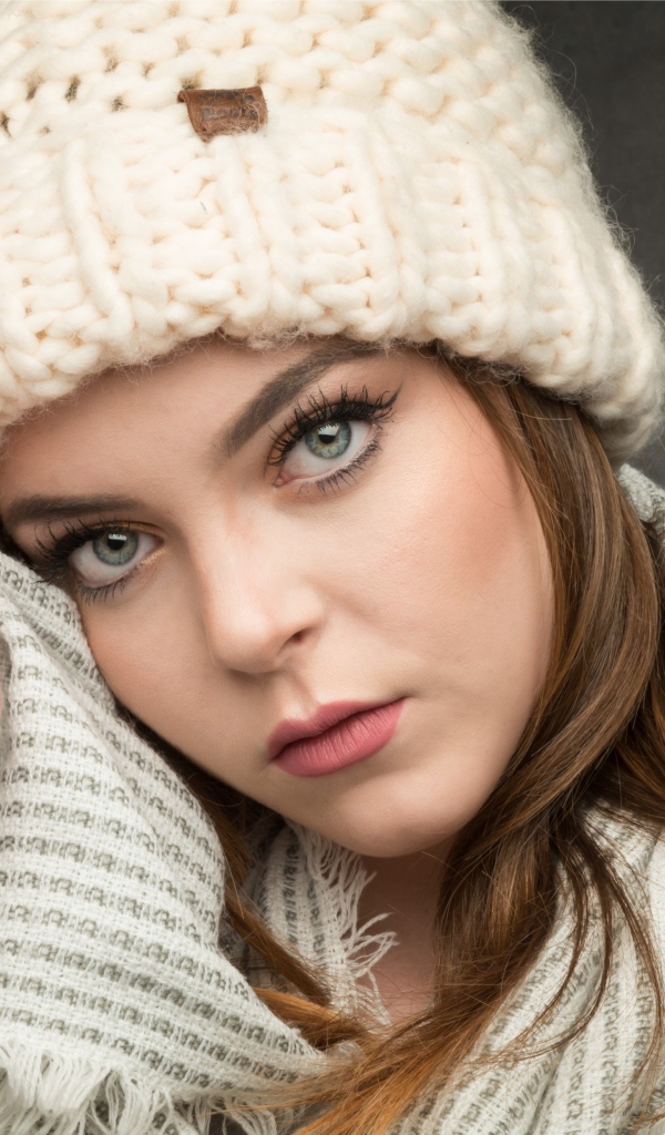 Красивая зеленоглазая девушка в белой вязаной шапке с шарфом