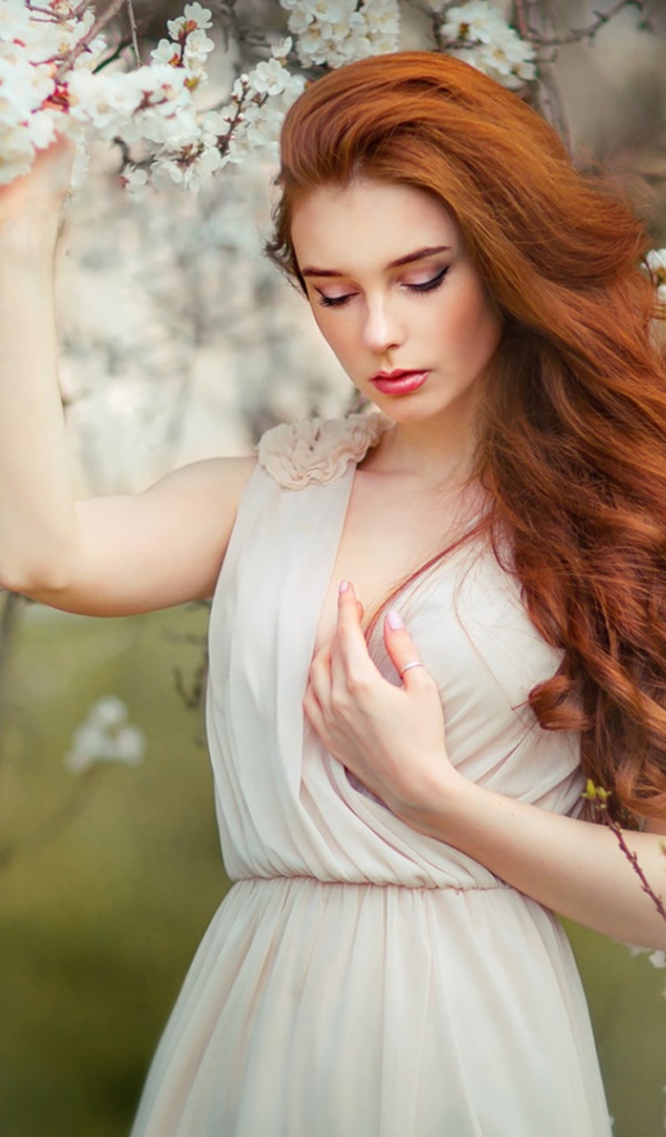 Красивая рыжеволосая девушка у цветущего дерева абрикоса 