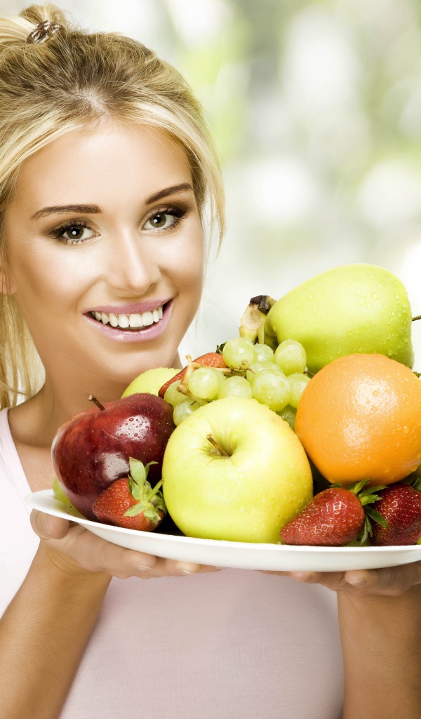Красивая улыбающаяся блондинка с тарелкой с фруктами в руках