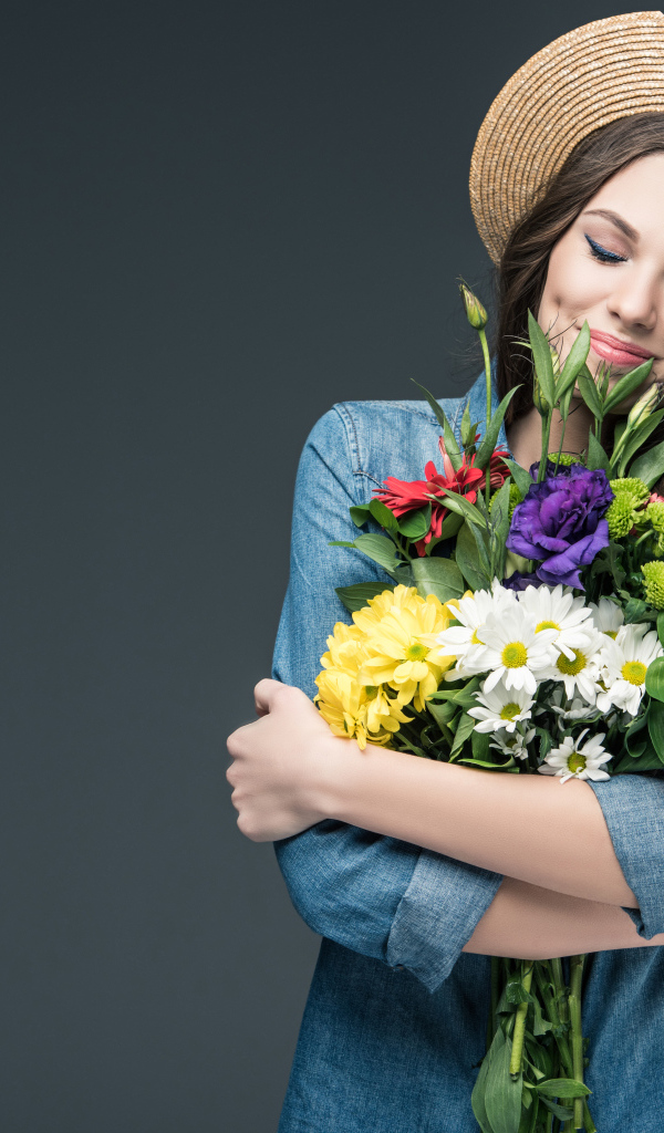 Красивая улыбающаяся девушка в шляпе с букетом цветов