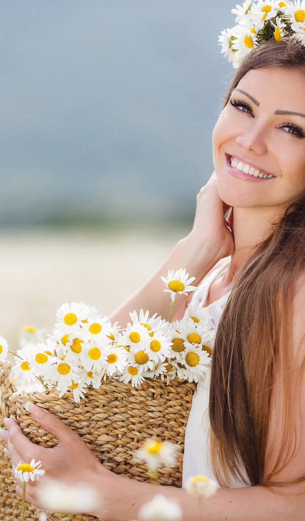 Красивая улыбающаяся девушка на поле с корзиной ромашек