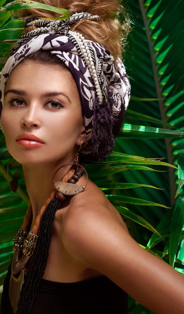 Красивая женщина в тюрбане с украшениями среди зеленых пальмовых листьев