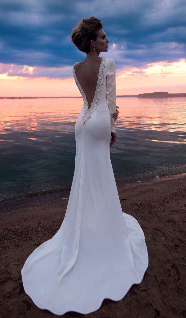 Красивая молодая девушка в свадебном платье у воды на закате 