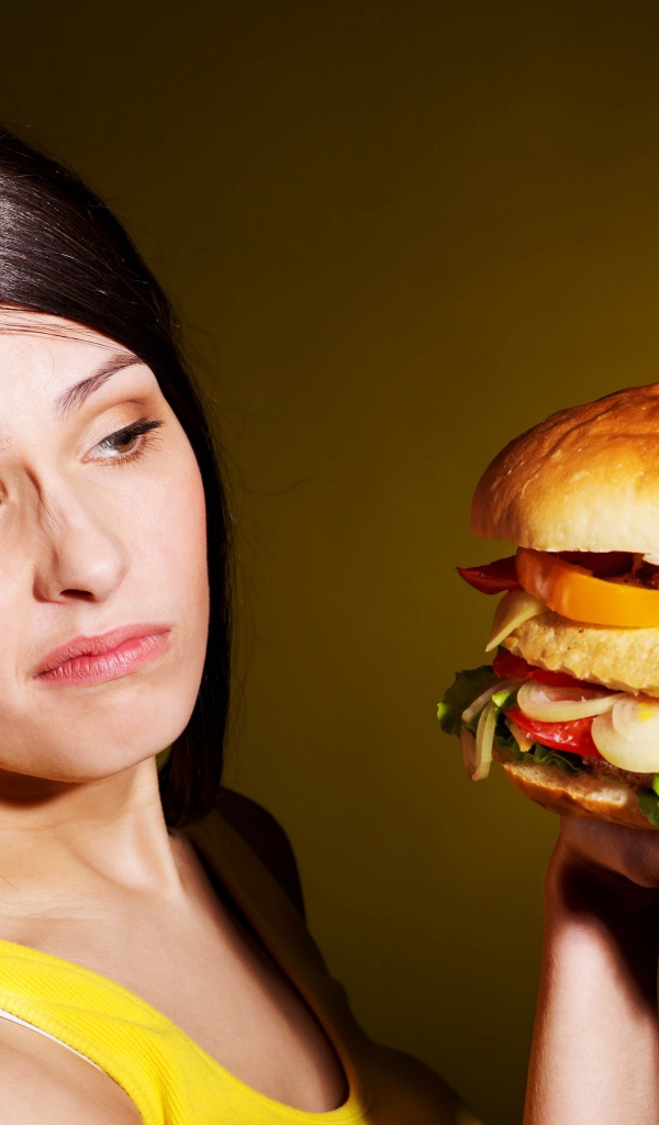 Недовольная девушка с большим гамбургером в руках 