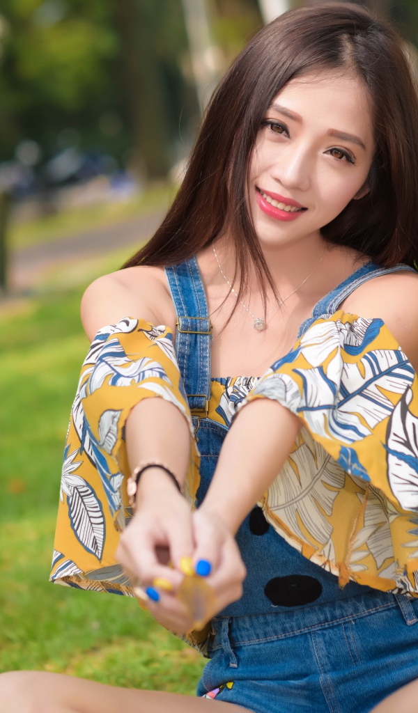 Улыбающаяся девушка азиатка сидит на траве