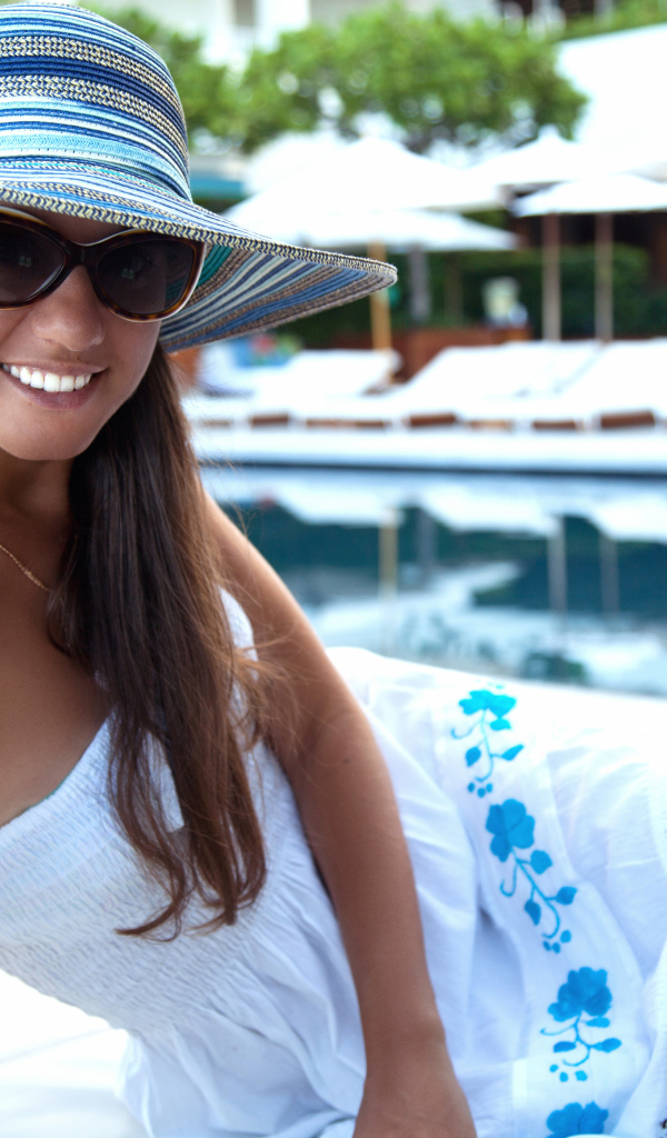 Улыбающаяся девушка в солнечных очках и шляпе у бассейна 