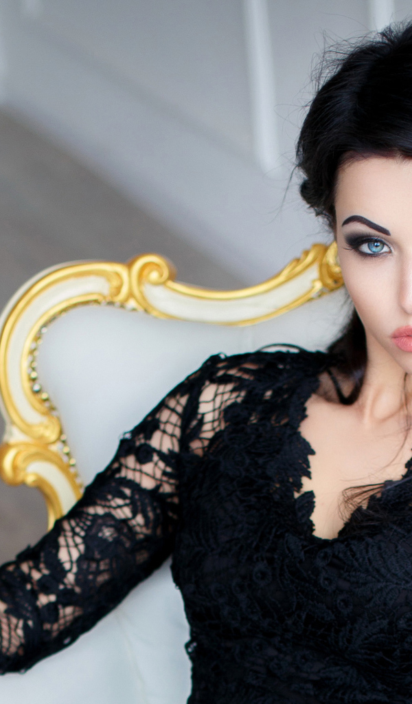 Эффектная брюнетка в черном платье сидит в кресле