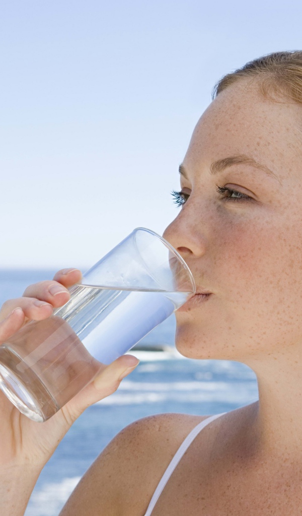 Девушка пьет воду со стакана на фоне моря
