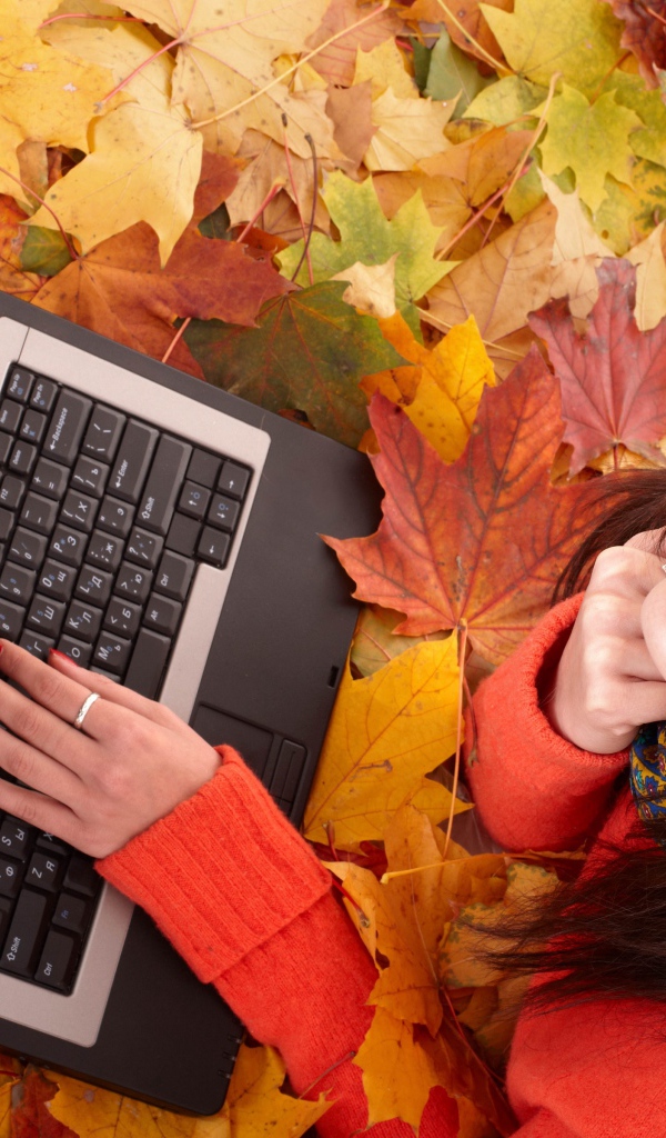 Девушка лежит на сухой опавшей листве с ноутбуком осенью