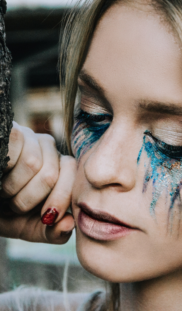 Заплаканная блондинка стоит у дерева