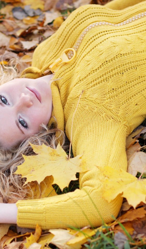 Молодая блондинка лежит на сухой листве осенью