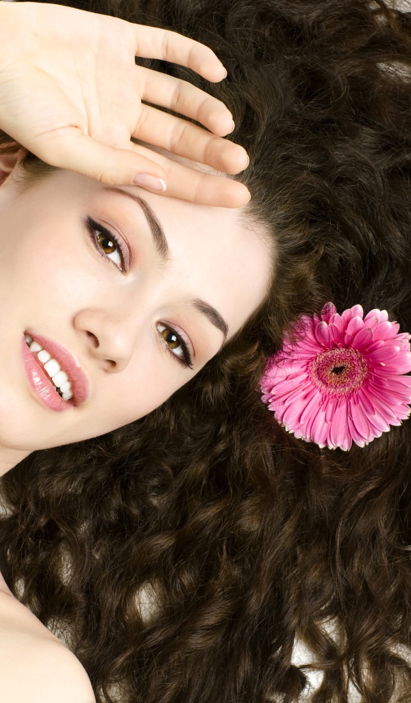Молодая шатенка с розовым цветком герберы в волосах
