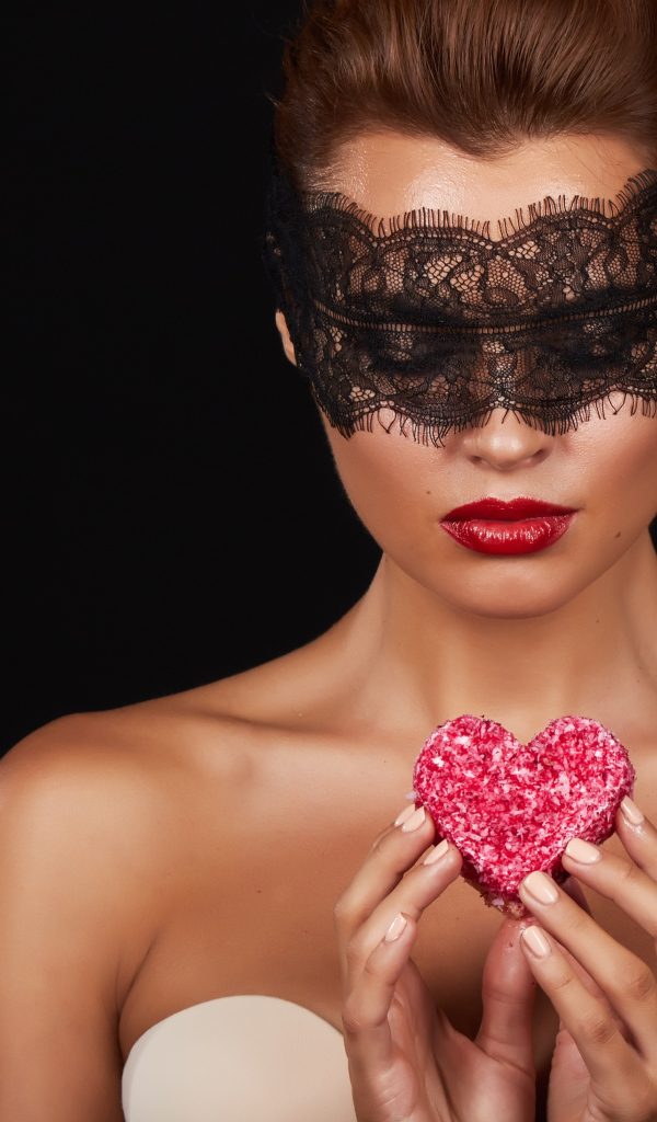 Молодая девушка в черной маске с красным сердцем в руках