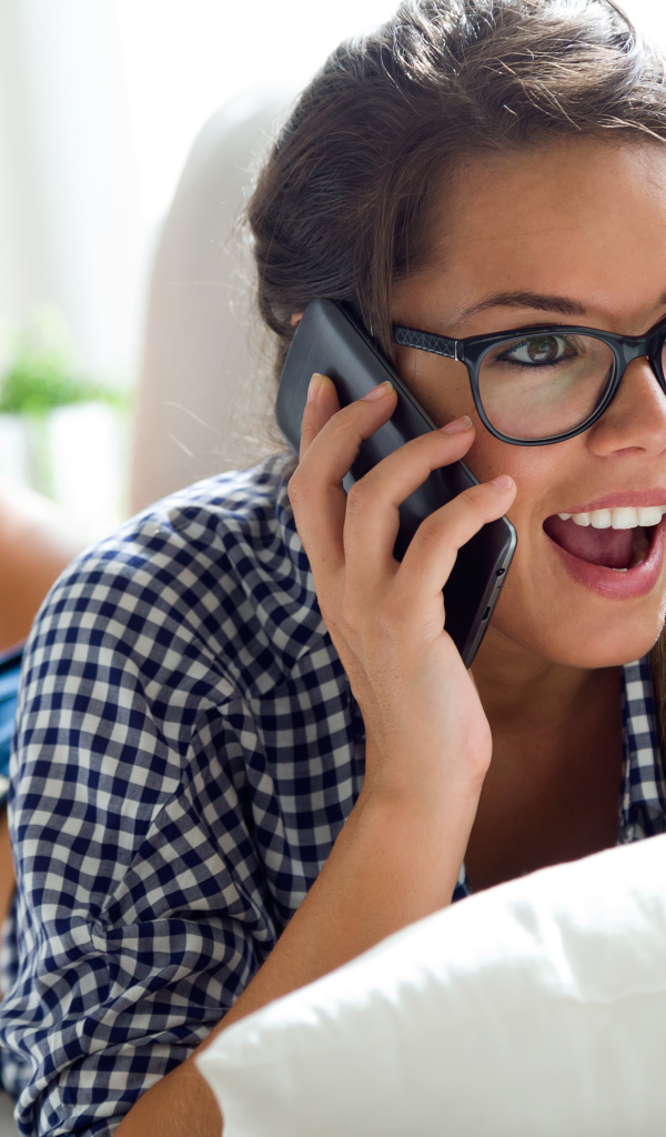 Молодая девушка в очках на диване разговаривает по смартфону