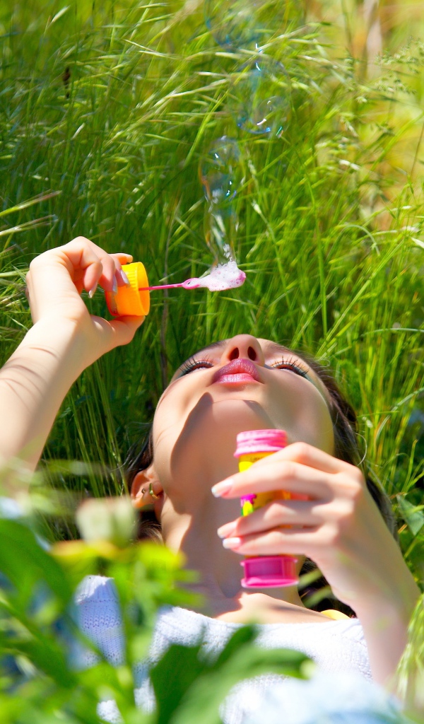 Молодая девушка лежит на зеленой траве с мыльными пузырями