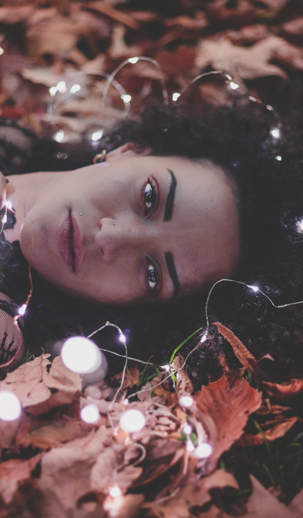 Молодая девушка лежит с гирляндой на желтых листьях