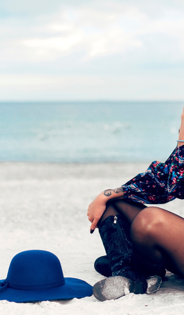 Молодая девушка с синей шляпой сидит на пляже