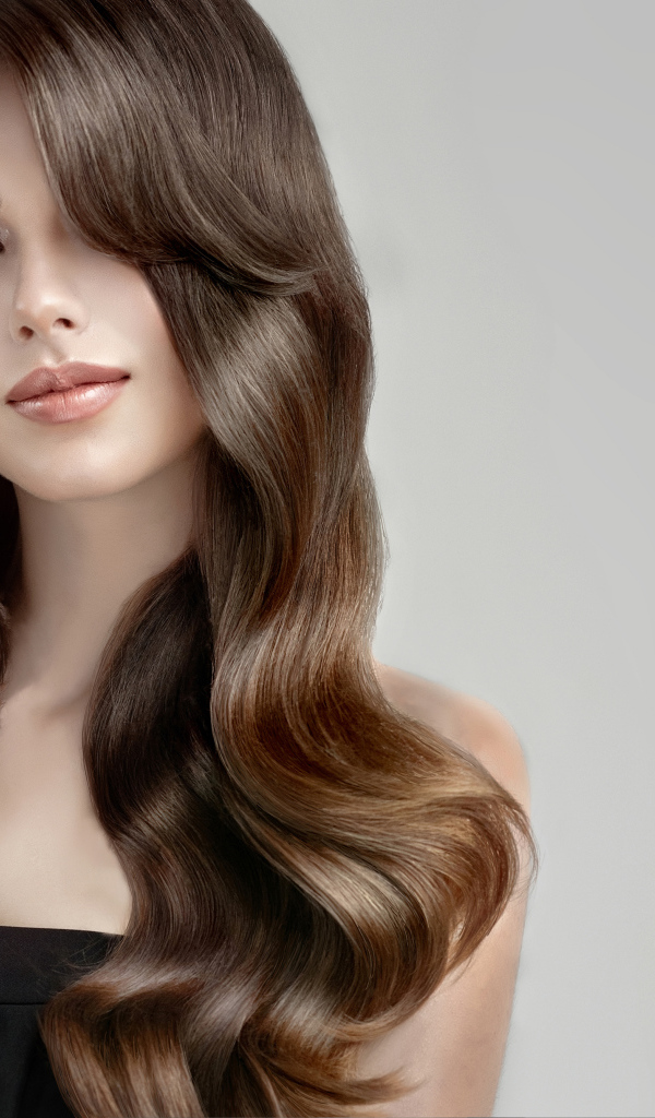 Молодая девушка с красивыми длинными волосами на сером фоне