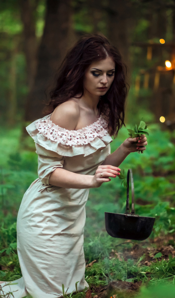 Молодая девушка колдунья варит зелье в лесу