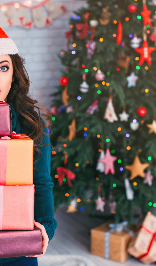 Удивленная девушка с подарками у новогодней елки 