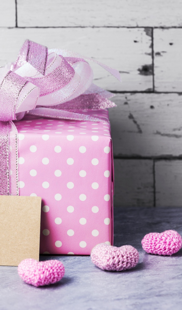 Большая сиреневая подарочная коробка с бантом и маленькими сердечками на фоне стены