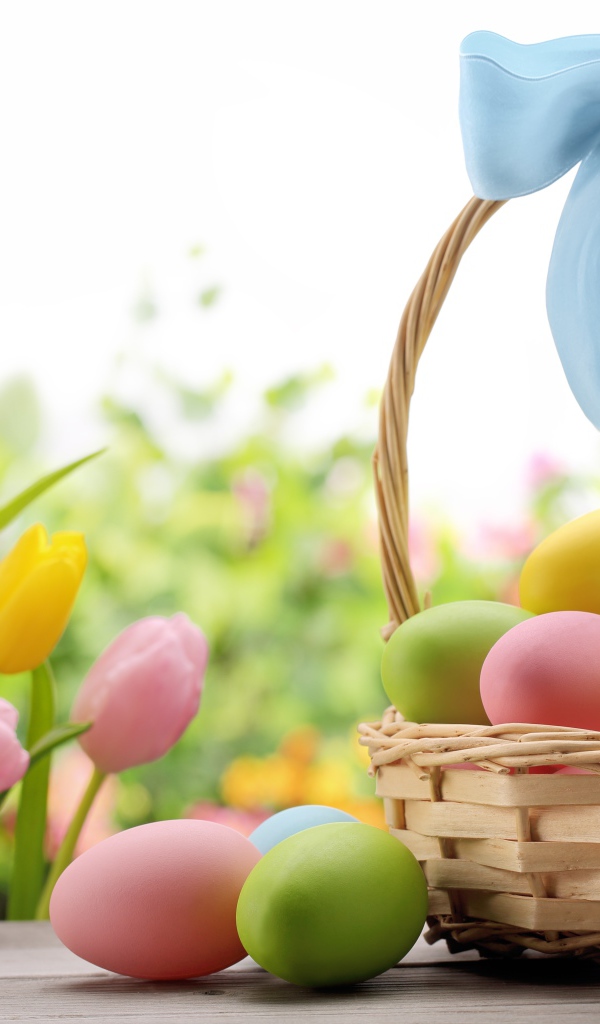 Корзина крашеных яиц с голубым бантом  на фоне тюльпанов на  Пасху