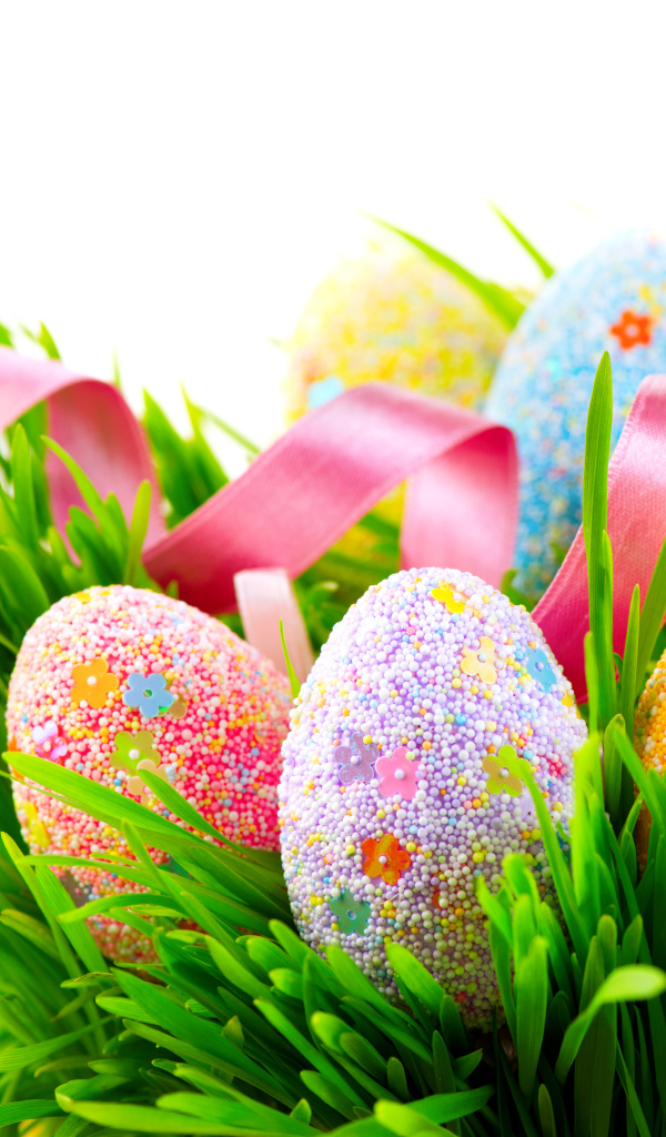 Пасхальные яйца в зеленой траве с розовой лентой на белом фоне