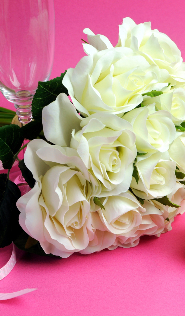 Букет белых роз, пирожное и два бокала на розовом фоне на 8 марта