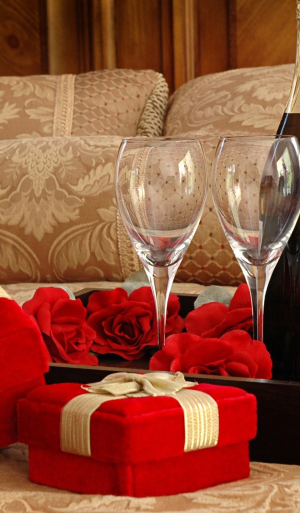 Бутылка вина, два бокала и подарки для романтического вечера на кровати 