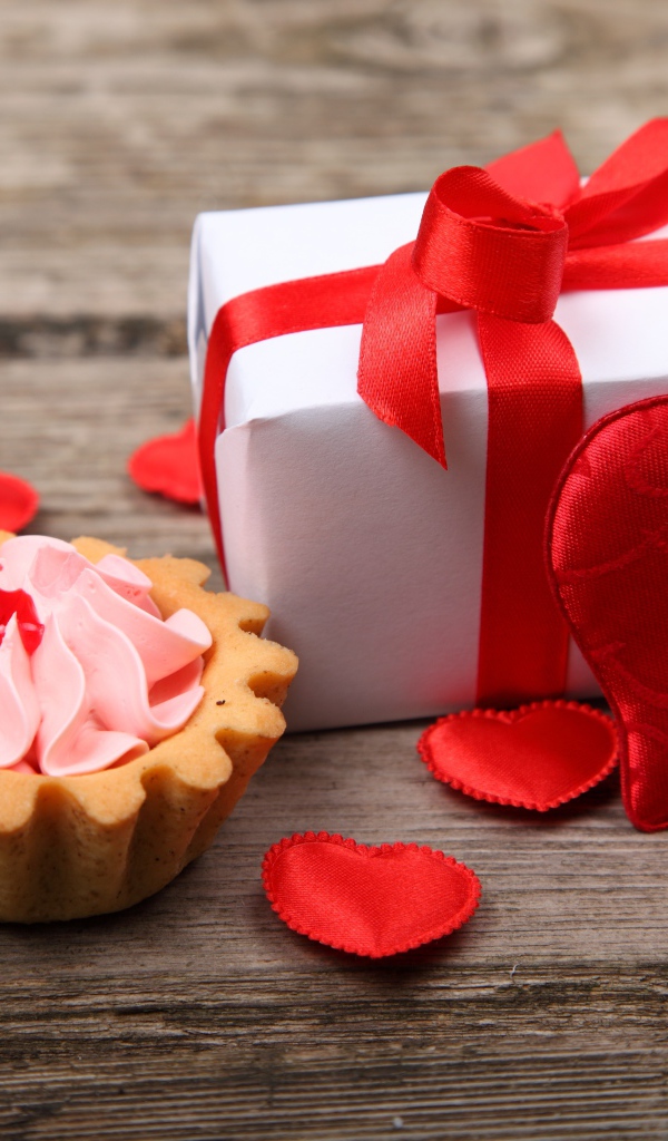 Подарок с красными сердечками и пирожным на столе