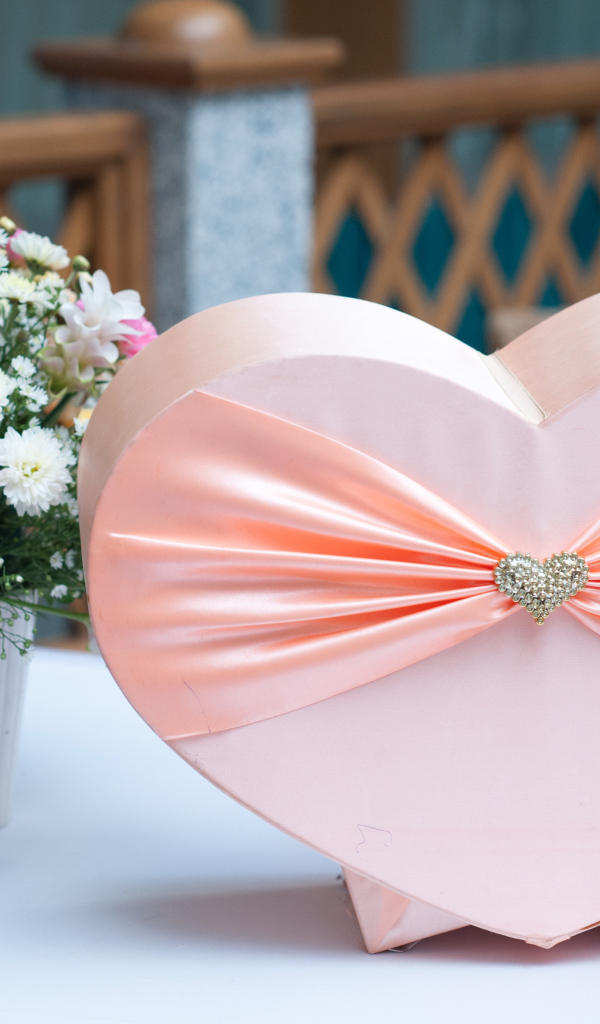 Большая розовая коробка в форме сердца на столе с букетом хризантем