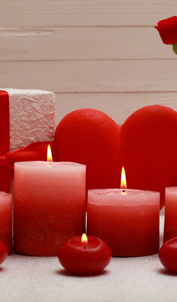 Зажженные красные свечи на столе с подарком, красным сердцем и цветами в вазе 