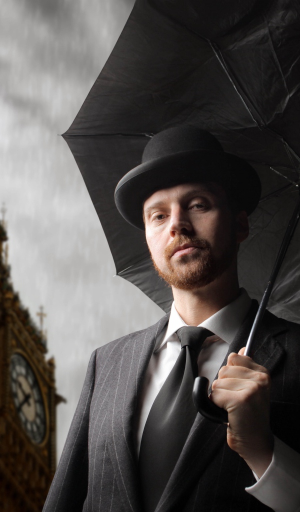 Мужчина в костюме с черным зонтом у башни с часами 