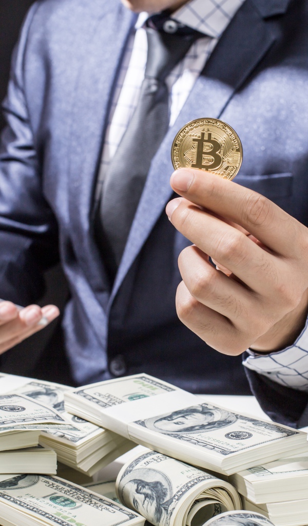 Мужчина с пачками долларов и монетой биткоин в руке