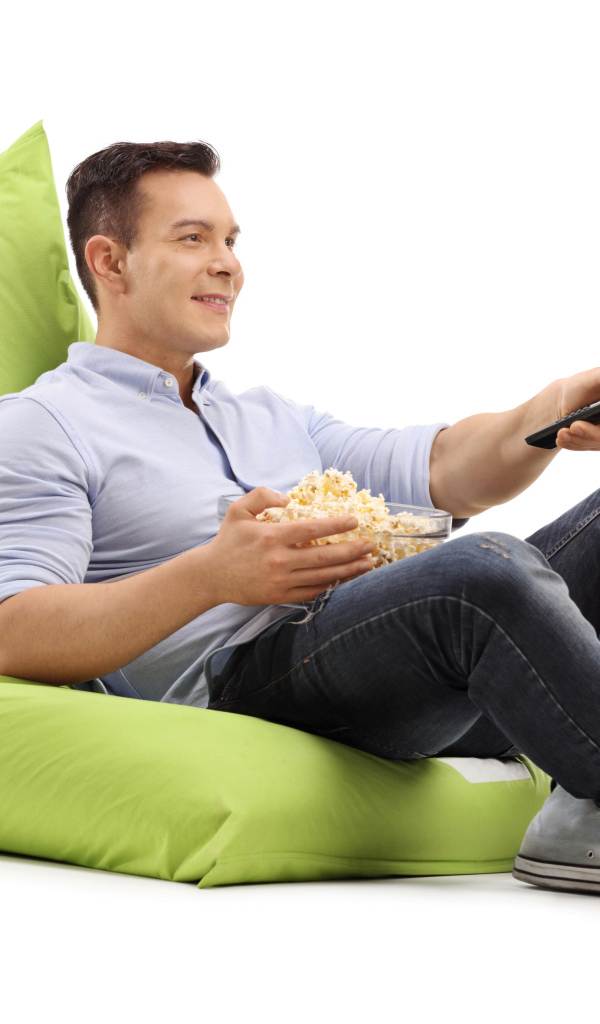 Мужчина с попкорном и пультом от телевизора лежит на зеленой подушке
