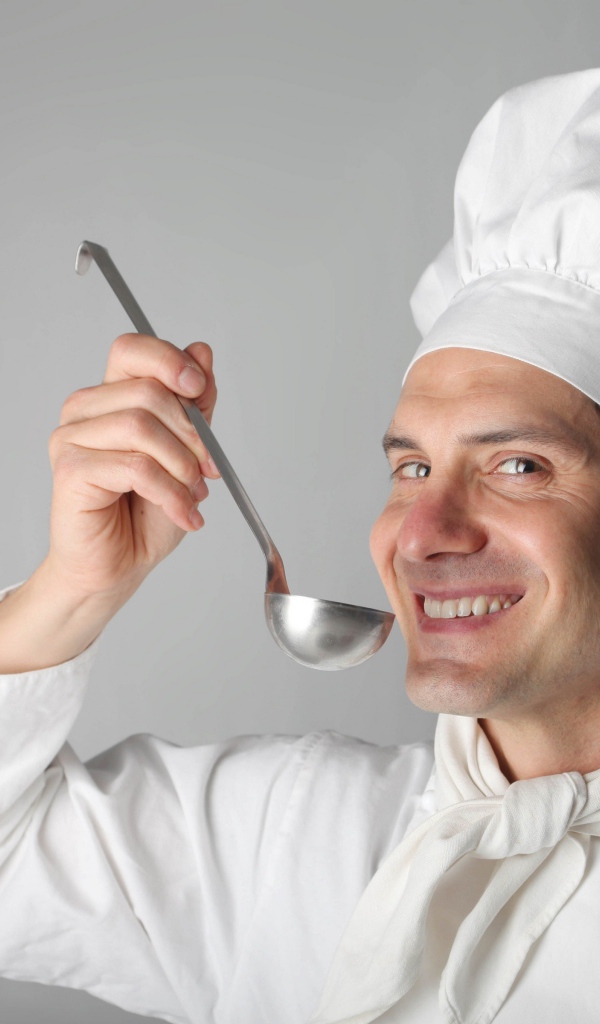 Smiling male cook with a ladle in his hands on a gray background