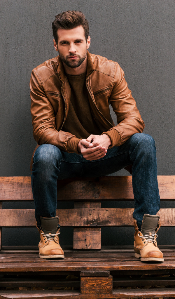 Молодой красивый мужчина сидит на деревянной лавке